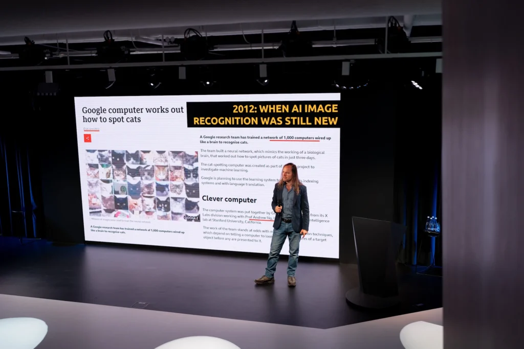 Мерайн Маркус на конференції виступає зі сцени з мікрофоном на фоні презентації