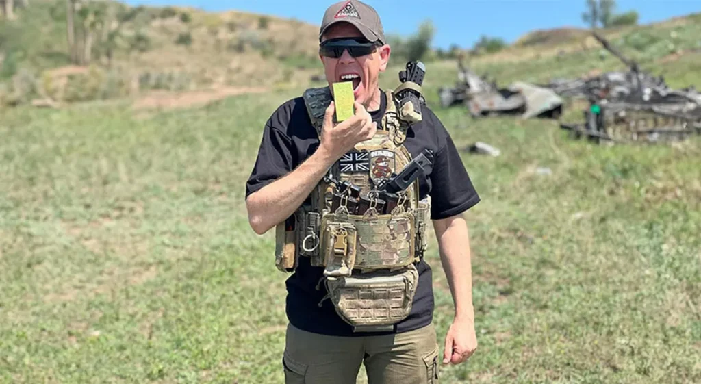 Man in military uniform wearing body armor against a grassy background