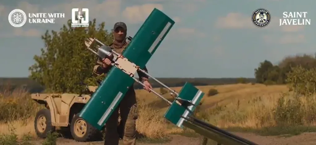 A soldier holds a drone in an open field
